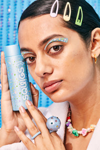 An image of a girl with hair clips holding a blue bottle of hair oil.